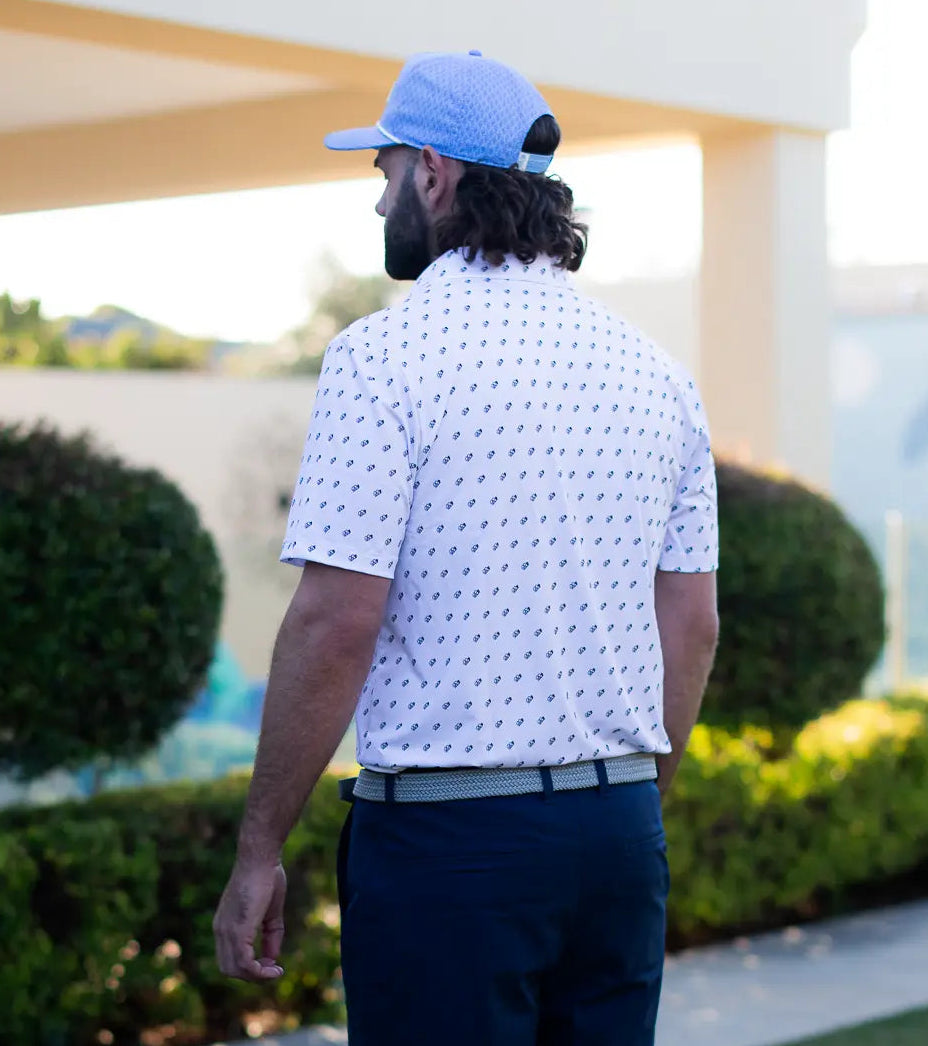 Man wearing a white patterned shirt and blue cap walking on a golf course.