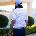 Man wearing a white patterned shirt and blue cap walking on a golf course.