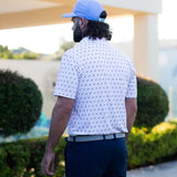 Man wearing a white patterned shirt and blue cap walking on a golf course.