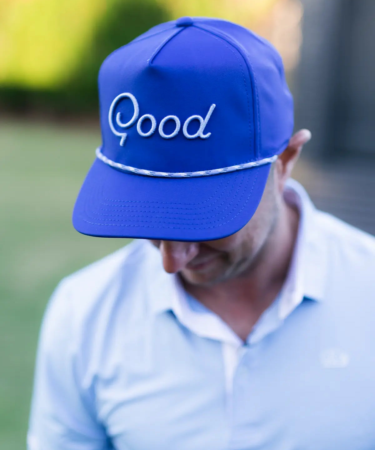 Person wearing a blue cap with 'Good' embroidered on it, outdoors.
