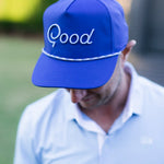 Person wearing a blue cap with 'Good' embroidered on it, outdoors.