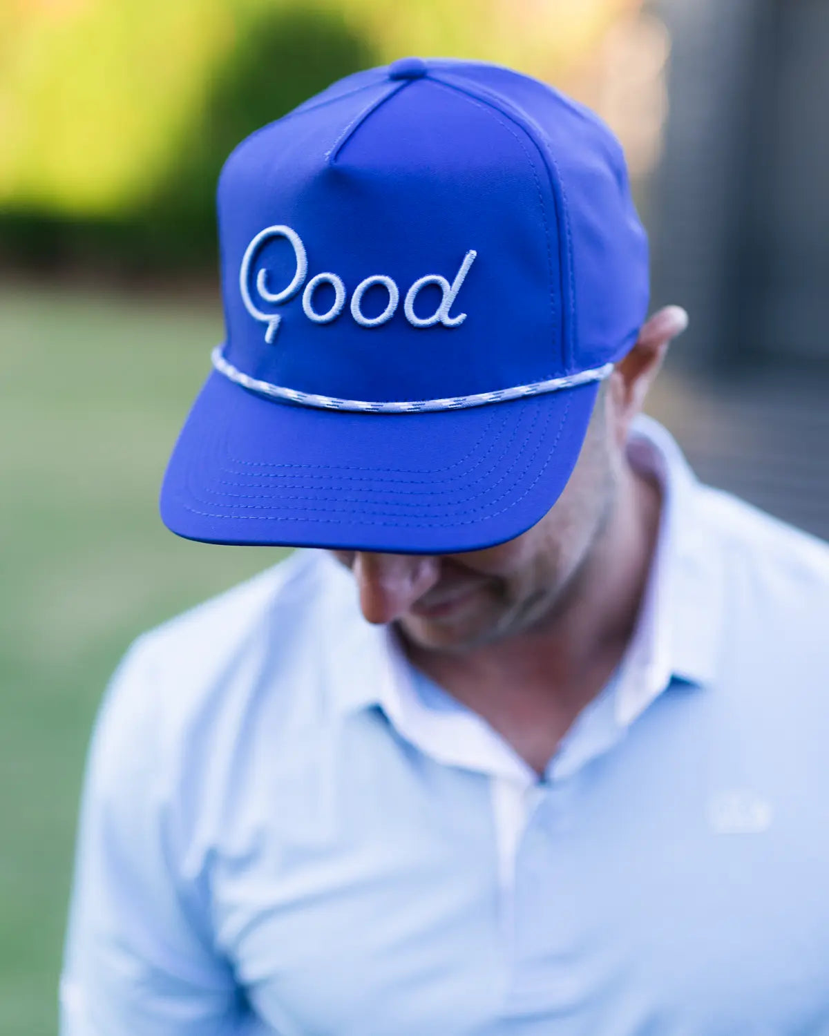 Person wearing a blue cap with 'Good' embroidered on it, outdoors.