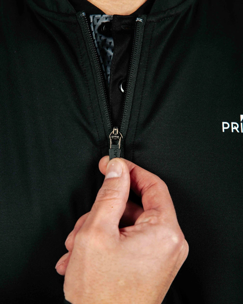Hand zipping a black jacket with a brand logo on a dark background