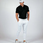 Man wearing a black polo shirt, white pants, and a white cap on a gray background