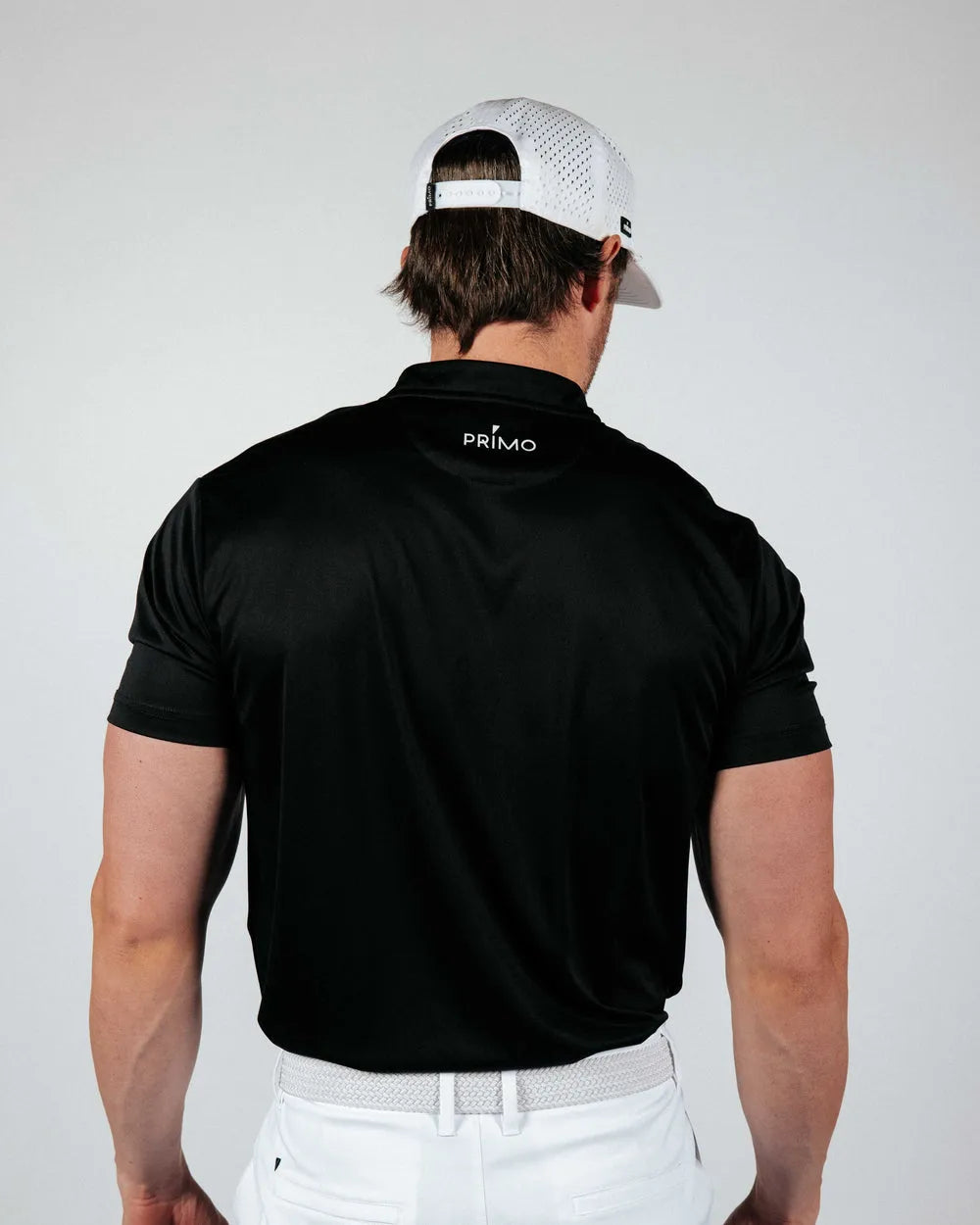 Man wearing a black Primo polo shirt and white cap on a plain background
