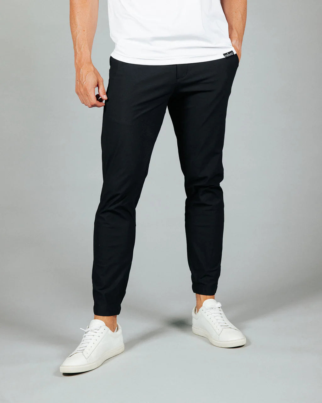 Person wearing black pants and white sneakers on a gray background