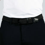 Person wearing a black woven belt with a silver buckle on dark pants against a white background