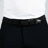 Person wearing a black woven belt with a silver buckle on dark pants against a white background