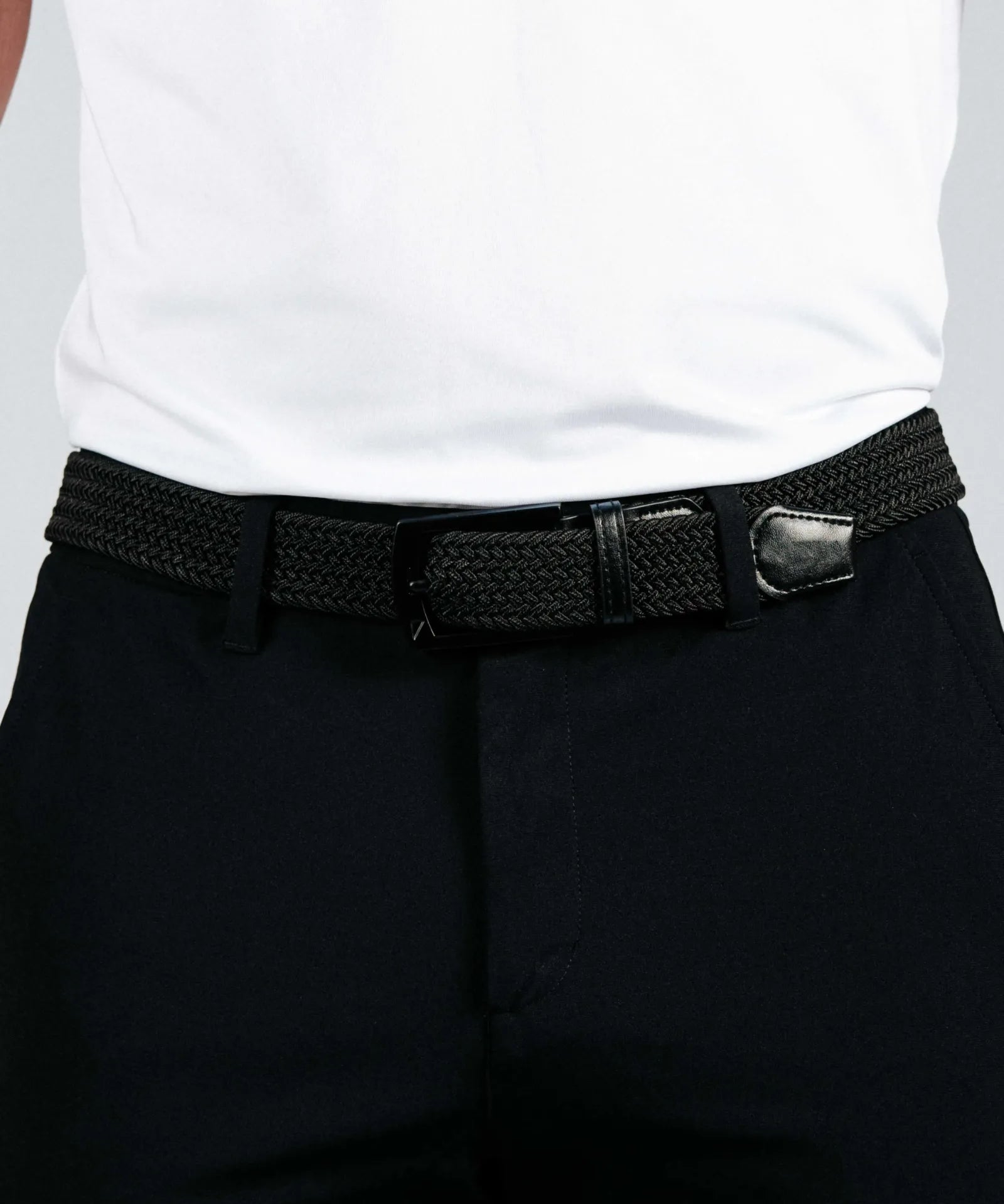 Person wearing a black woven belt with a silver buckle on dark pants against a white background