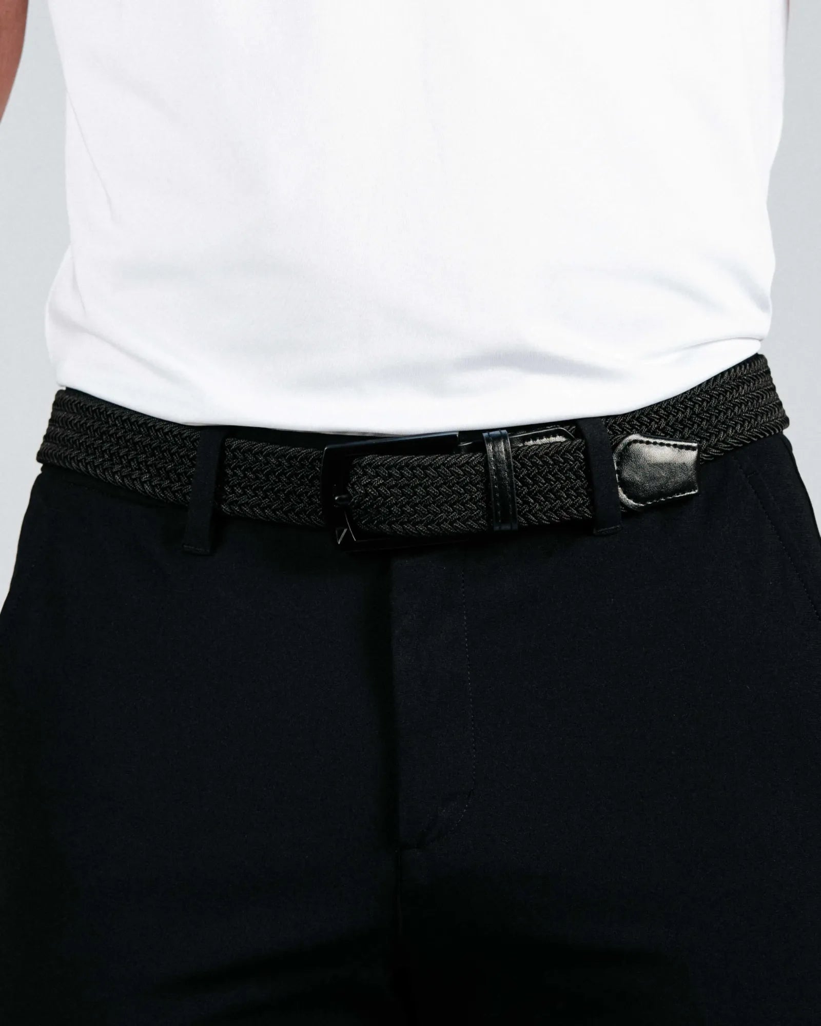 Person wearing a black woven belt with a silver buckle on dark pants against a white background