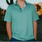 Man wearing a green patterned shirt standing in front of a cactus and desert landscape.