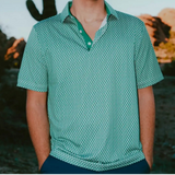 Man wearing a green patterned shirt standing in front of a cactus and desert landscape.