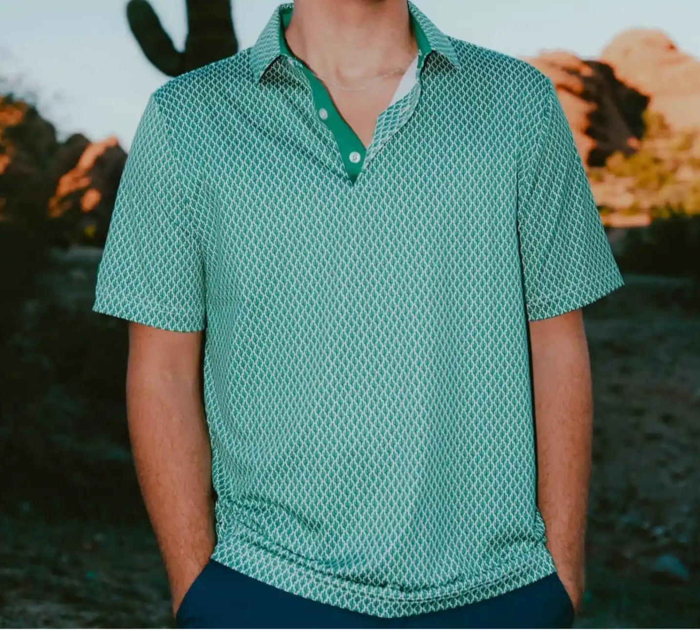 Man wearing a green patterned shirt standing in front of a cactus and desert landscape.