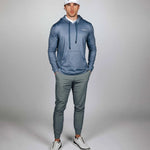 Man wearing a blue hoodie and gray pants with a white cap on a gray background