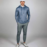 Man wearing a blue hoodie and gray pants with a white cap on a gray background