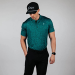 Man wearing a green patterned shirt, black pants, and a black cap on a gray background