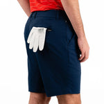 Person wearing navy shorts with a white golf glove in the pocket on a white background
