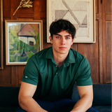 Man in a green polo shirt sitting on a couch with framed artwork in the background