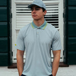 Man wearing a light blue polo shirt and cap standing in front of a white shutter.