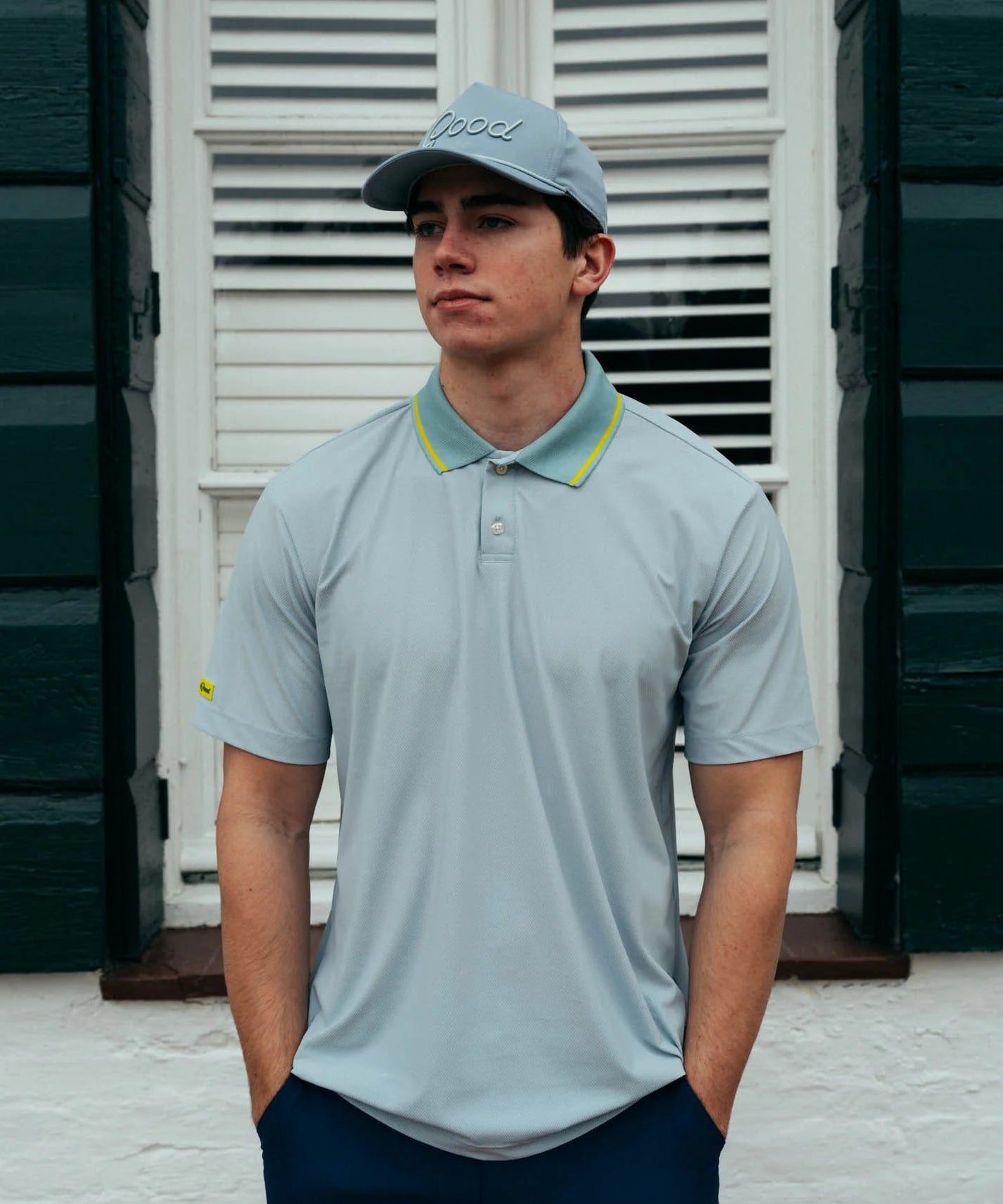 Man wearing a light blue polo shirt and cap standing in front of a white shutter.