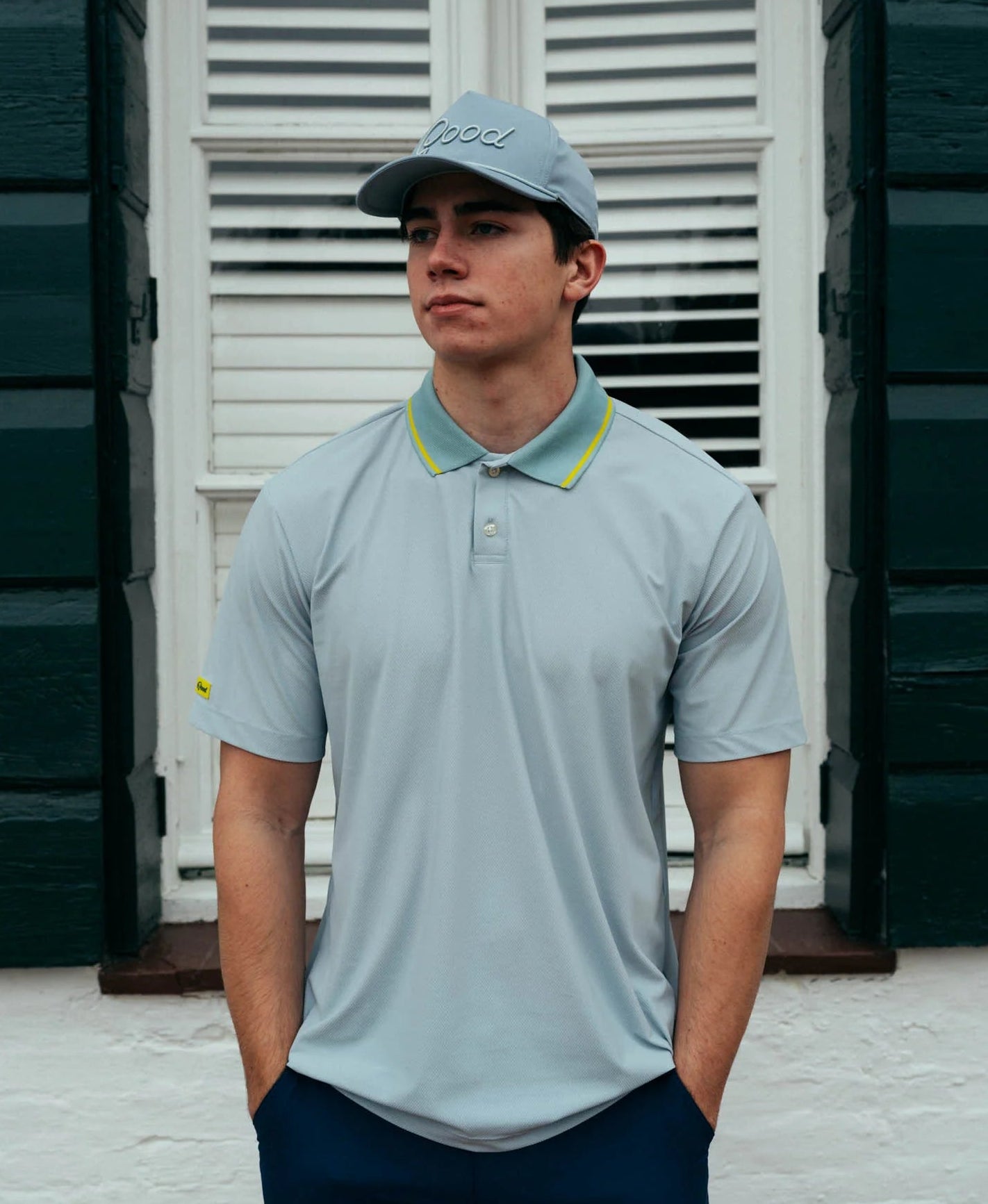Man wearing a light blue polo shirt and cap standing in front of a white shutter.