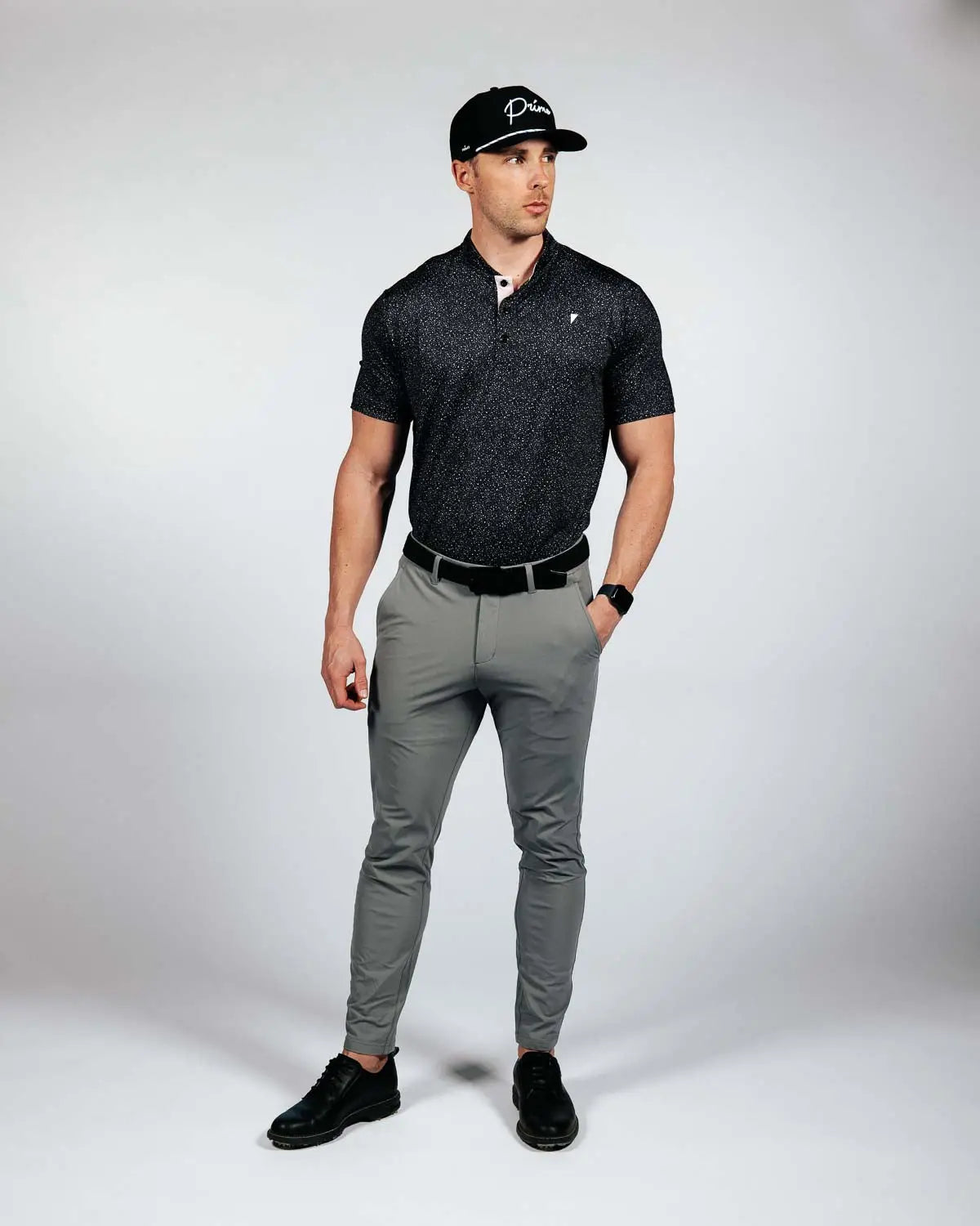 Man wearing a black polo shirt, gray pants, and black cap on a white background