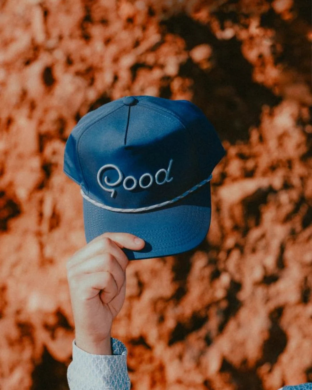Blue cap with 'Good' embroidered on it held against a blurred natural background