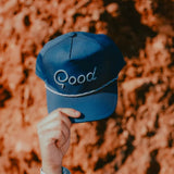 Blue cap with 'Good' embroidered on it held against a blurred natural background