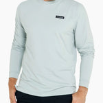 Man wearing a light blue long-sleeve shirt with a brand logo on a white background