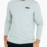 Man wearing a light blue long-sleeve shirt with a brand logo on a white background