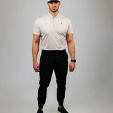 Man wearing a sand coloured polo shirt, black pants, and a white cap with a logo on a grey background