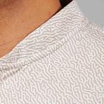 Close-up of a person wearing a beige patterned shirt with a neutral background