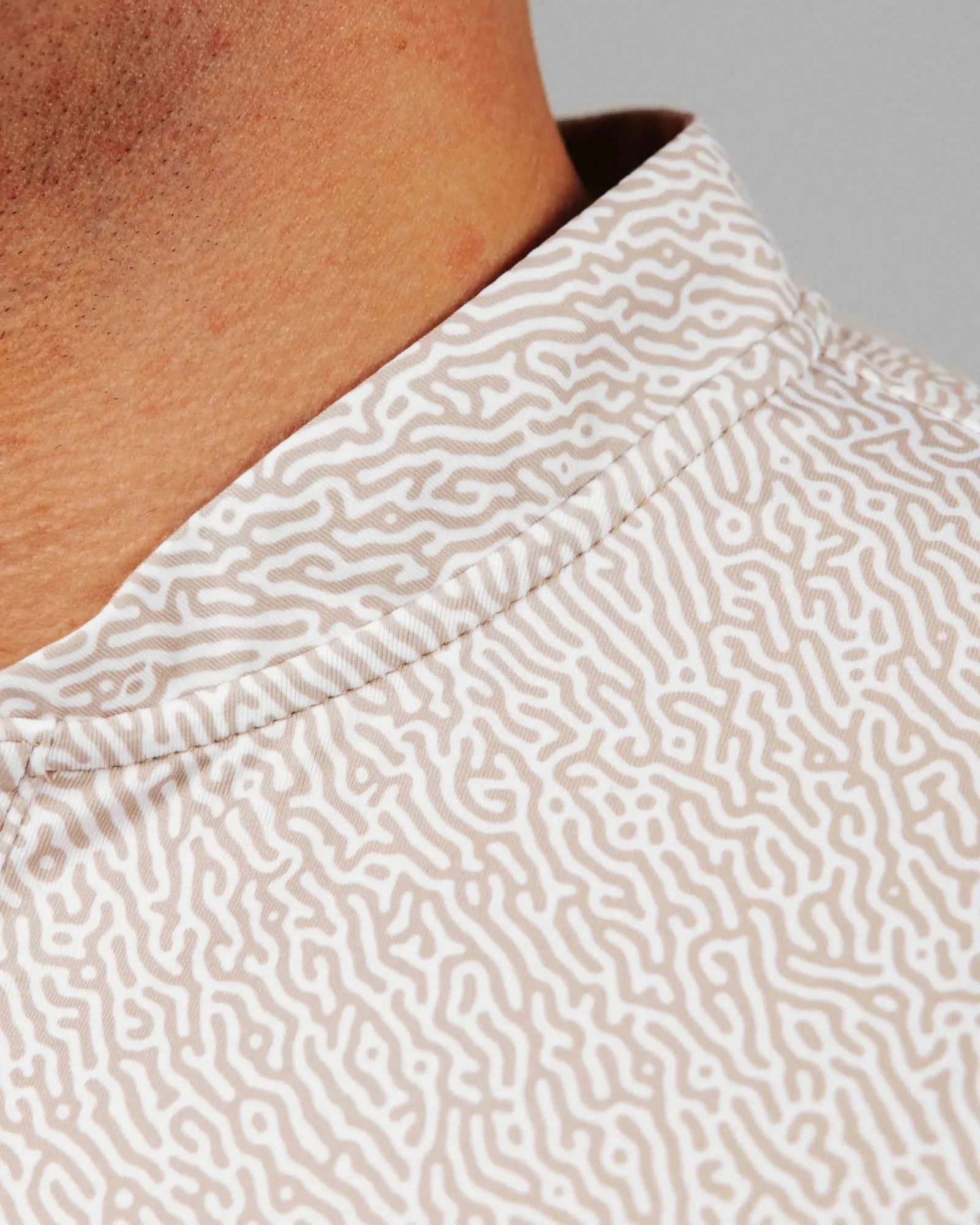 Close-up of a person wearing a beige patterned shirt with a neutral background