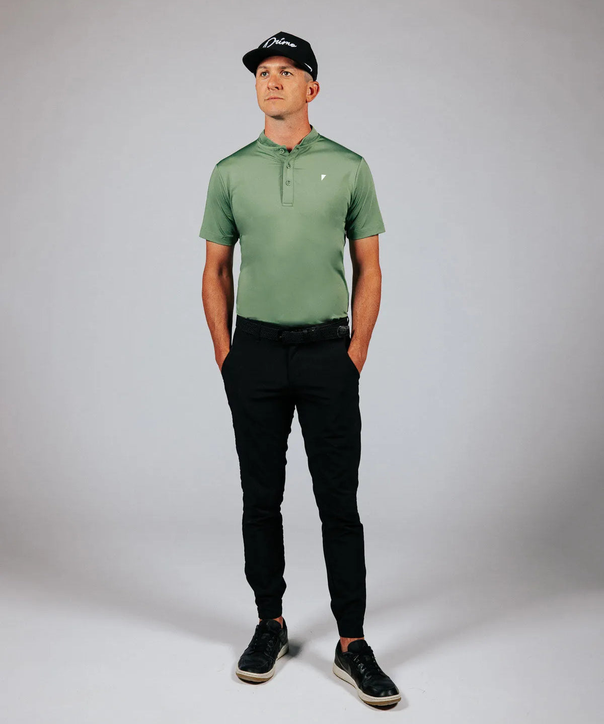 Man wearing a green polo shirt and black pants against a gray background