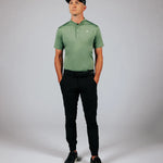 Man wearing a green polo shirt and black pants against a gray background