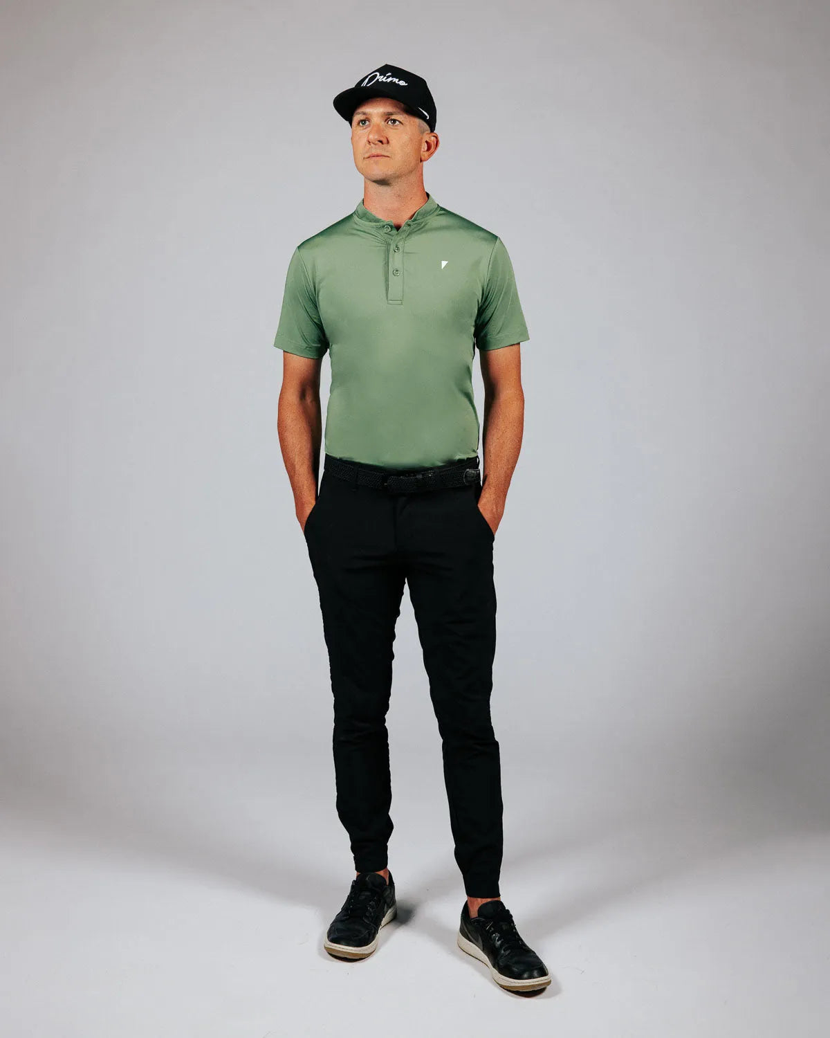 Man wearing a green polo shirt and black pants against a gray background