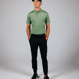 Man wearing a green polo shirt and black pants against a gray background