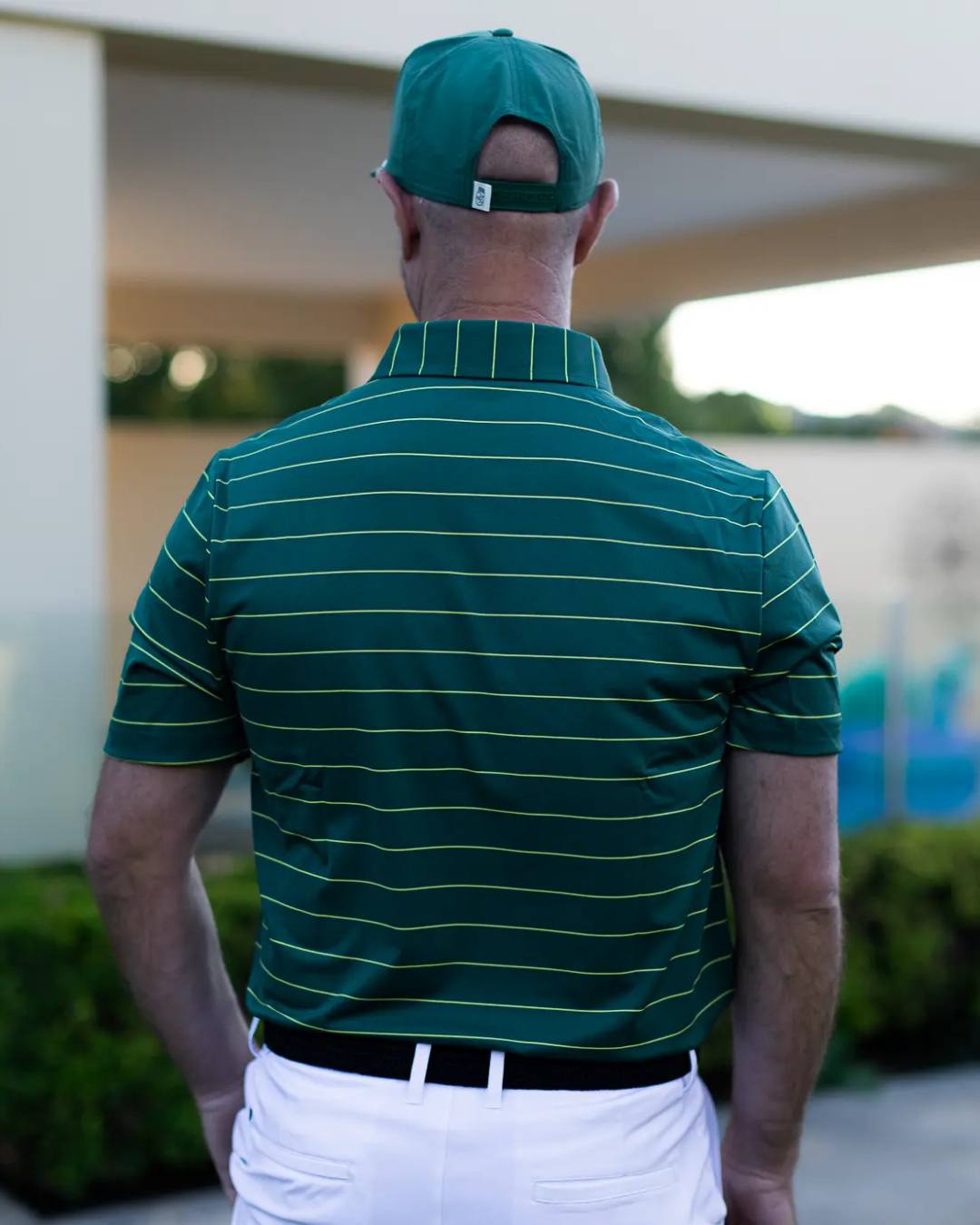 Man wearing a green striped polo shirt and cap, standing outdoors.
