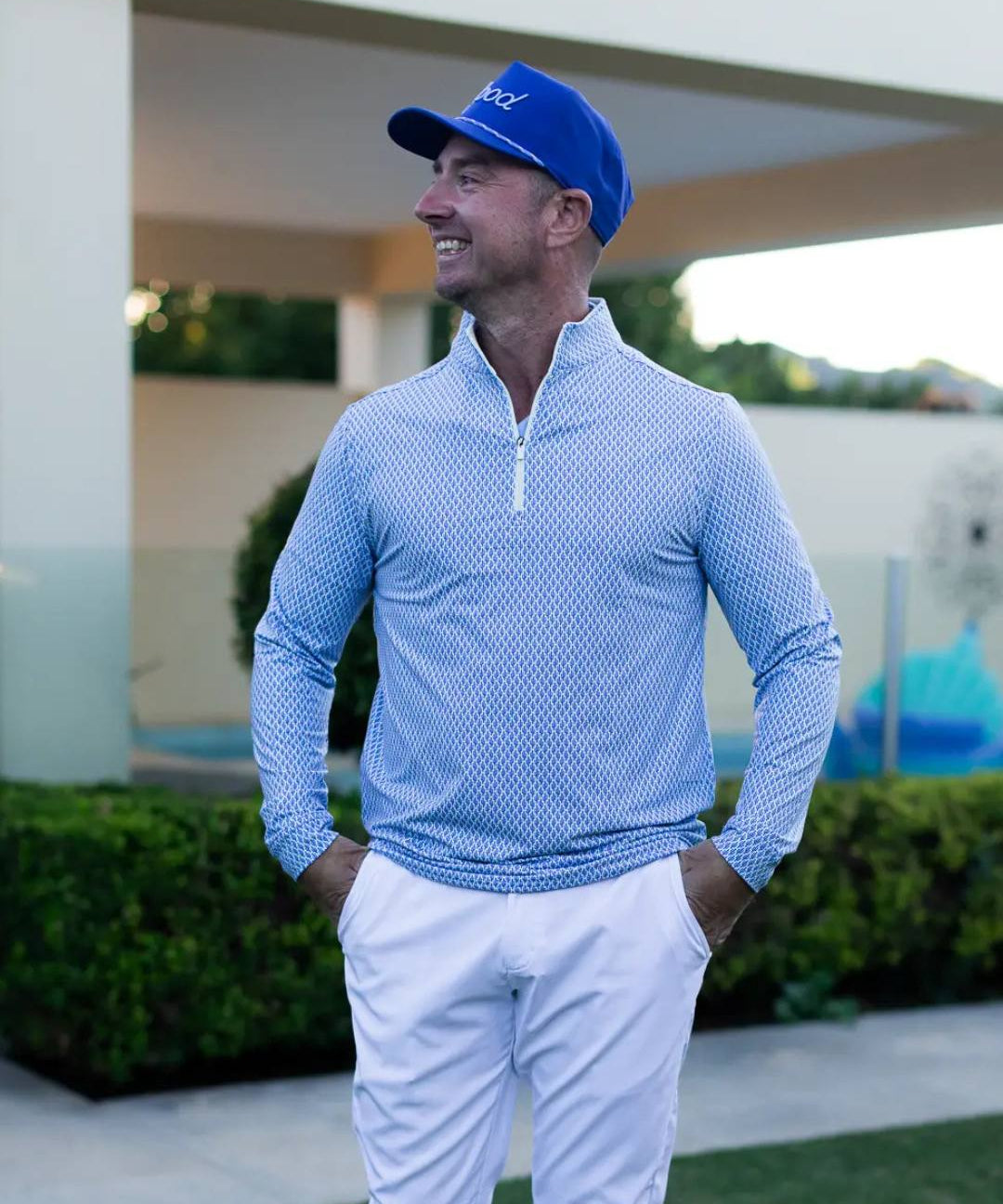 Man wearing a blue cap and light blue long-sleeve shirt with white pants, standing outdoors.