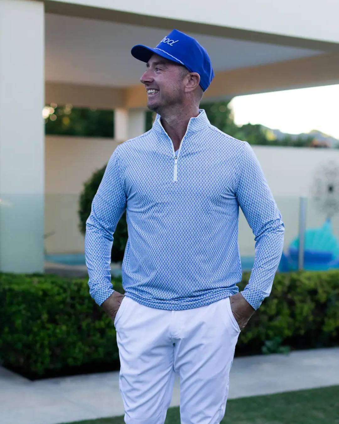 Man wearing a blue cap and light blue long-sleeve shirt with white pants, standing outdoors.