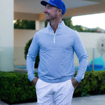 Man wearing a blue cap and light blue long-sleeve shirt with white pants, standing outdoors.