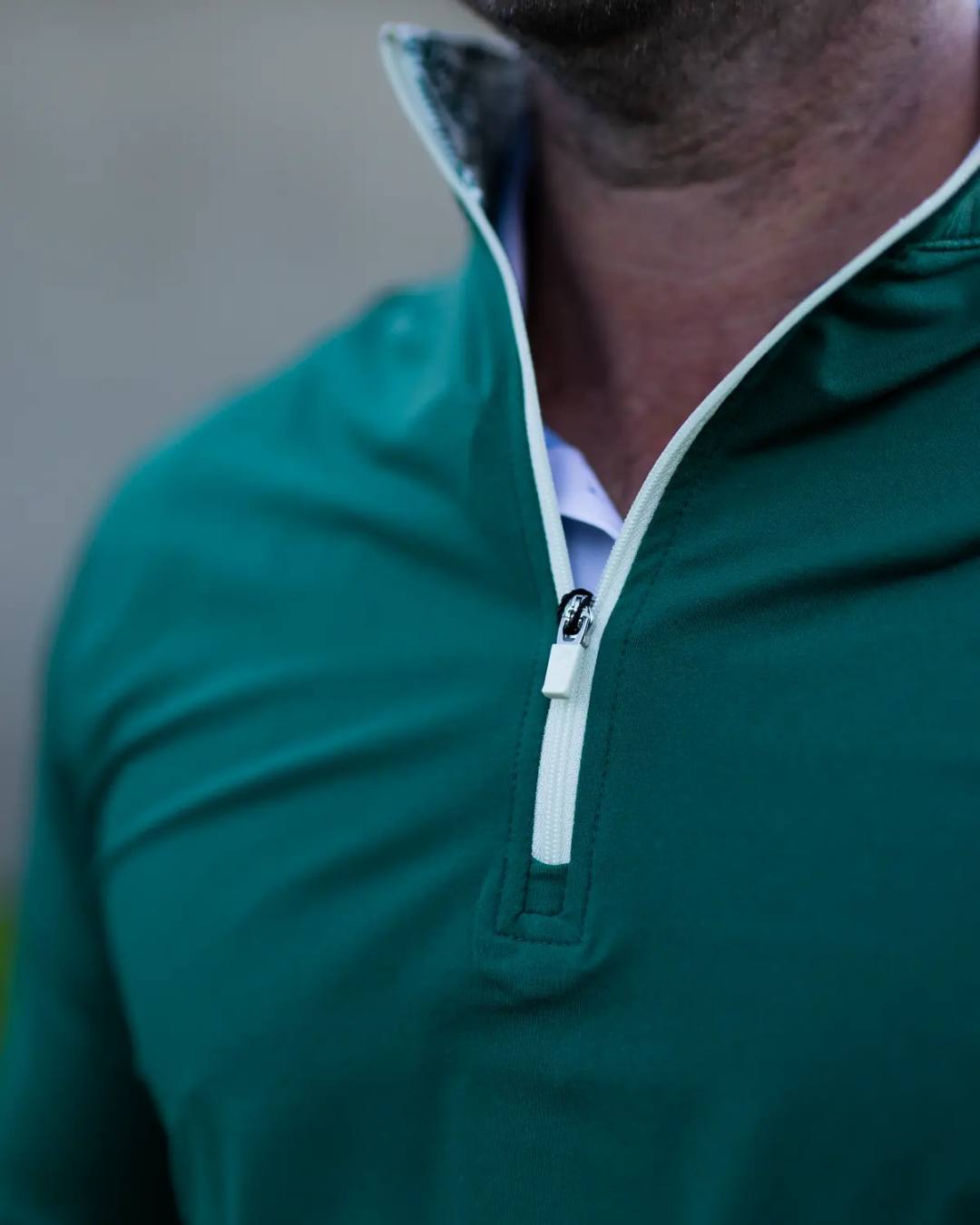 Close-up of a person wearing a green quarter-zip pullover with a blurred background