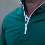 Close-up of a person wearing a green quarter-zip pullover with a blurred background