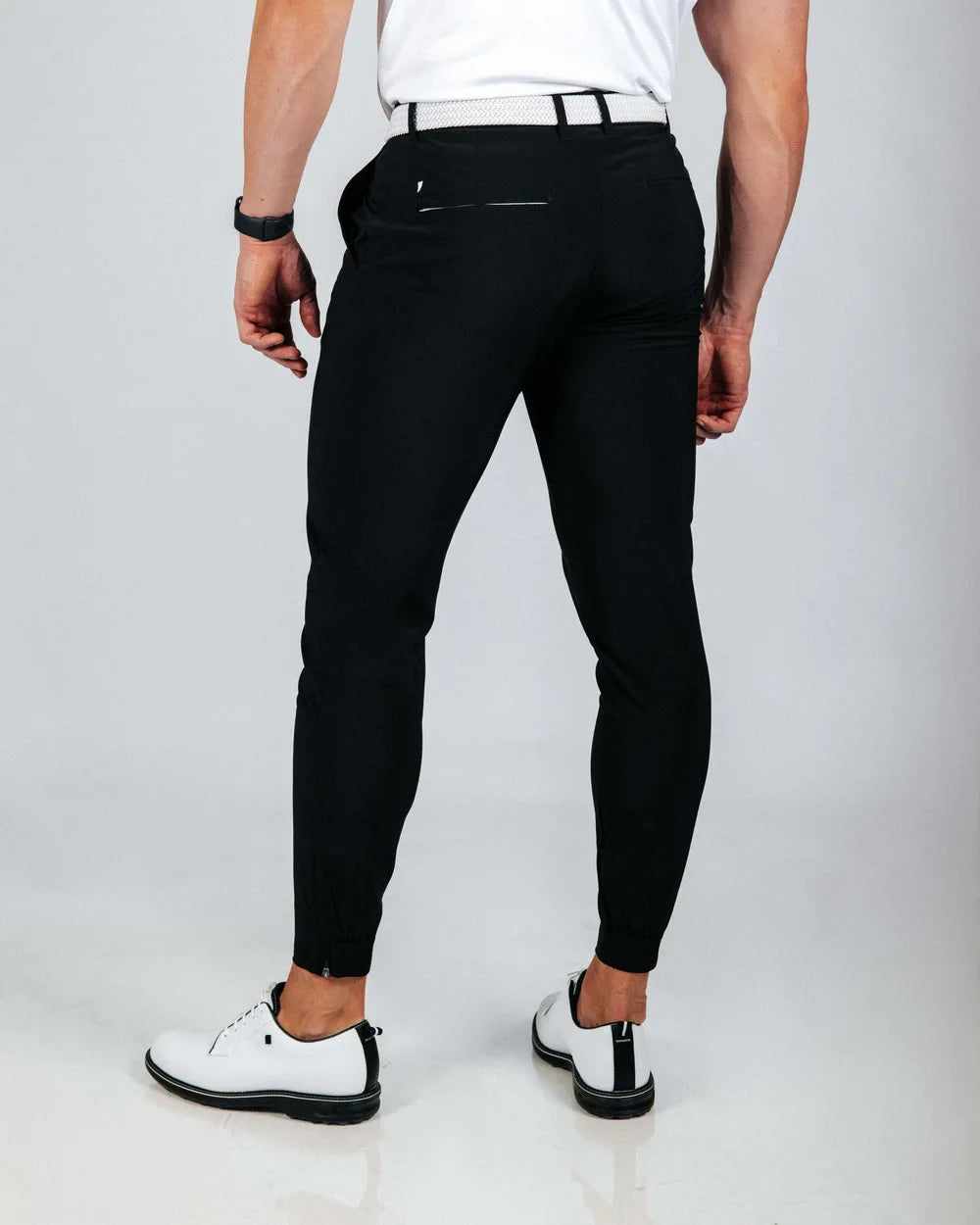 Person wearing black pants and white shoes on a light gray background