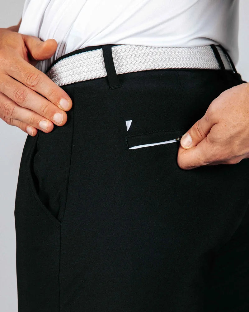 Person wearing black pants with a white belt and visible brand logo and back pocket zipper.