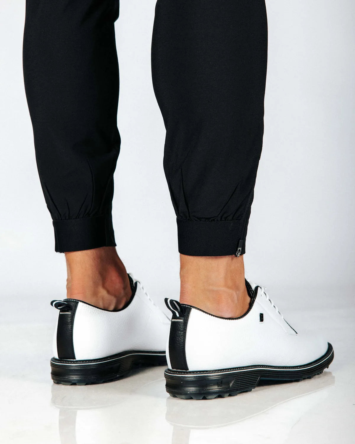 White shoes with black soles worn with black pants with cuff hem on a white background