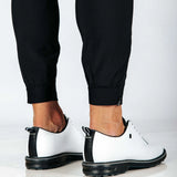 White shoes with black soles worn with black pants with cuff hem on a white background