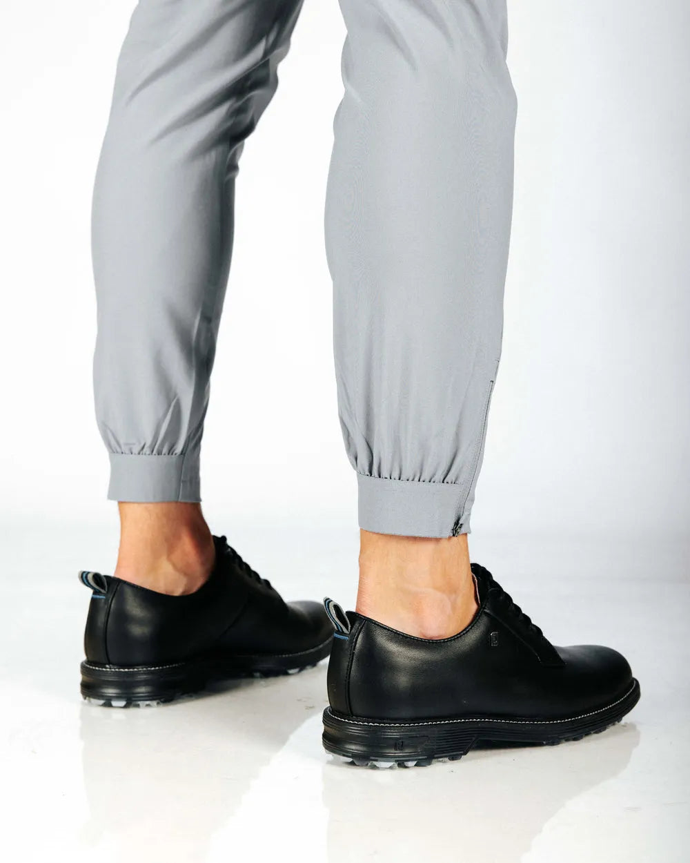 Person wearing black shoes and gray pants with a cuff hem on a white background