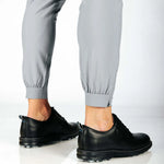 Person wearing black shoes and gray pants with a cuff hem on a white background
