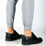 Person wearing black shoes and gray pants with a cuff hem on a white background